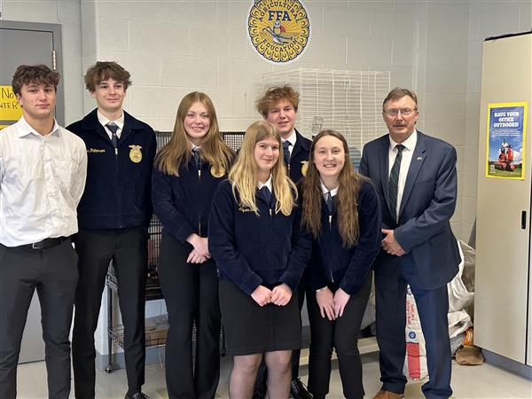 Middle and high school students stand together smiling next to the New York State Assemblyman in front of an FFA sign.
