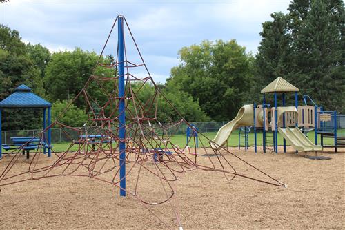 A school playground with a jungle gym, slides, benches and tables over new mulch.