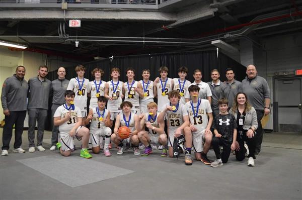 A high school boys basketball team smiles with medals, posing with their coaches.